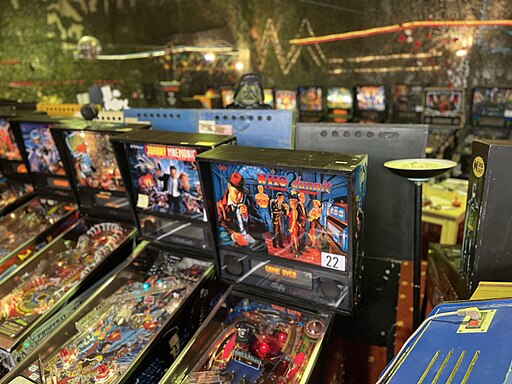 Colorful lineup of classic Midway pinball games in an arcade with black walls and neon wall decorations