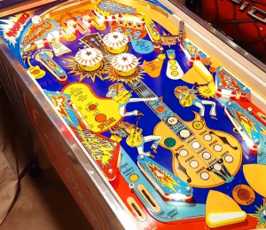 Playing field of the Nugent pinball machine, featuring a cobalt-blue background and an illustration of Ted Nugent's iconic guitar in the center, surrounded by flippers, bumpers, and lights.